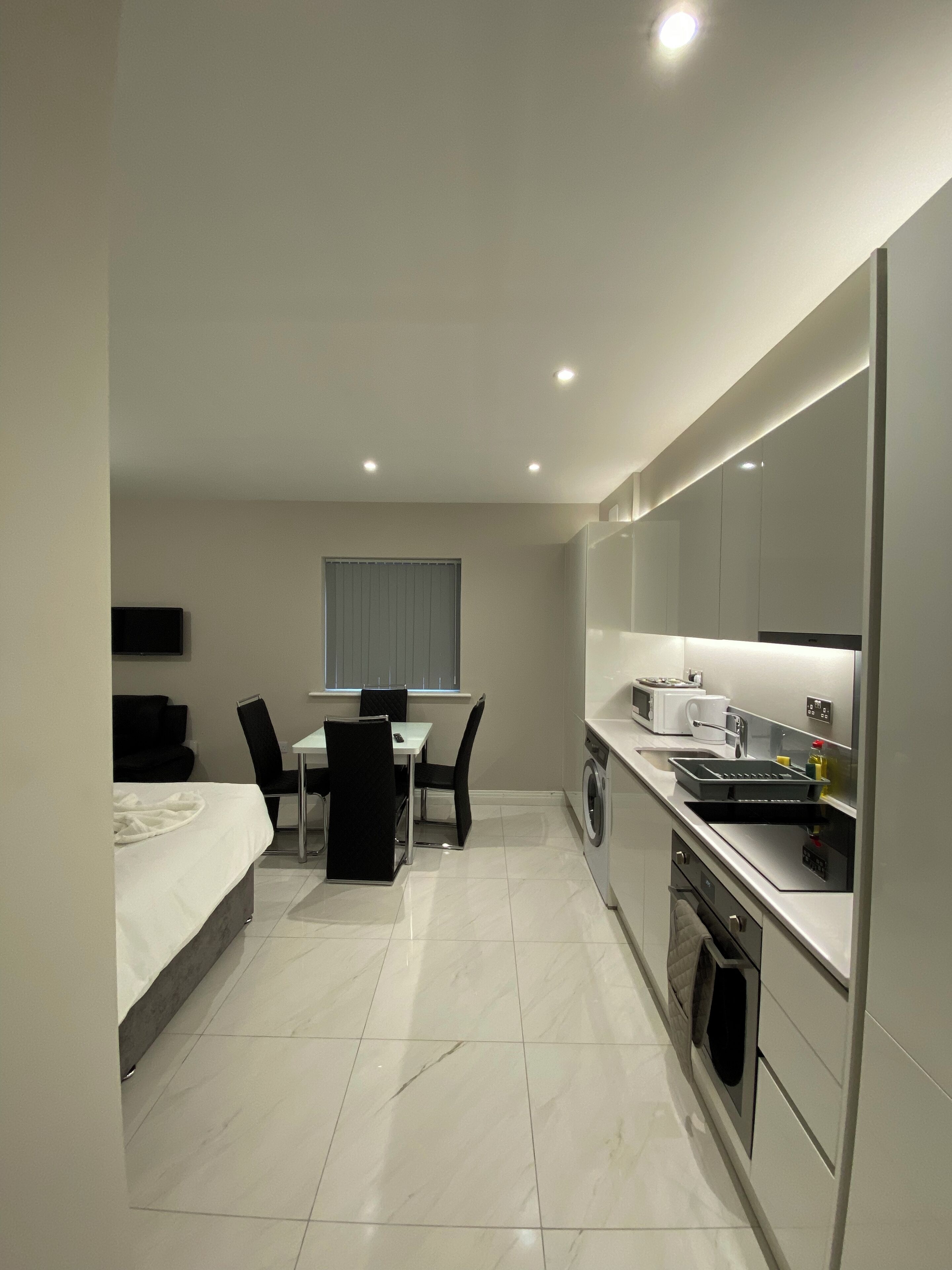 Une chambre d’hôtel moderne et compacte, comprenant un lit, un coin repas avec une table et des chaises, un lave-linge et une kitchenette.