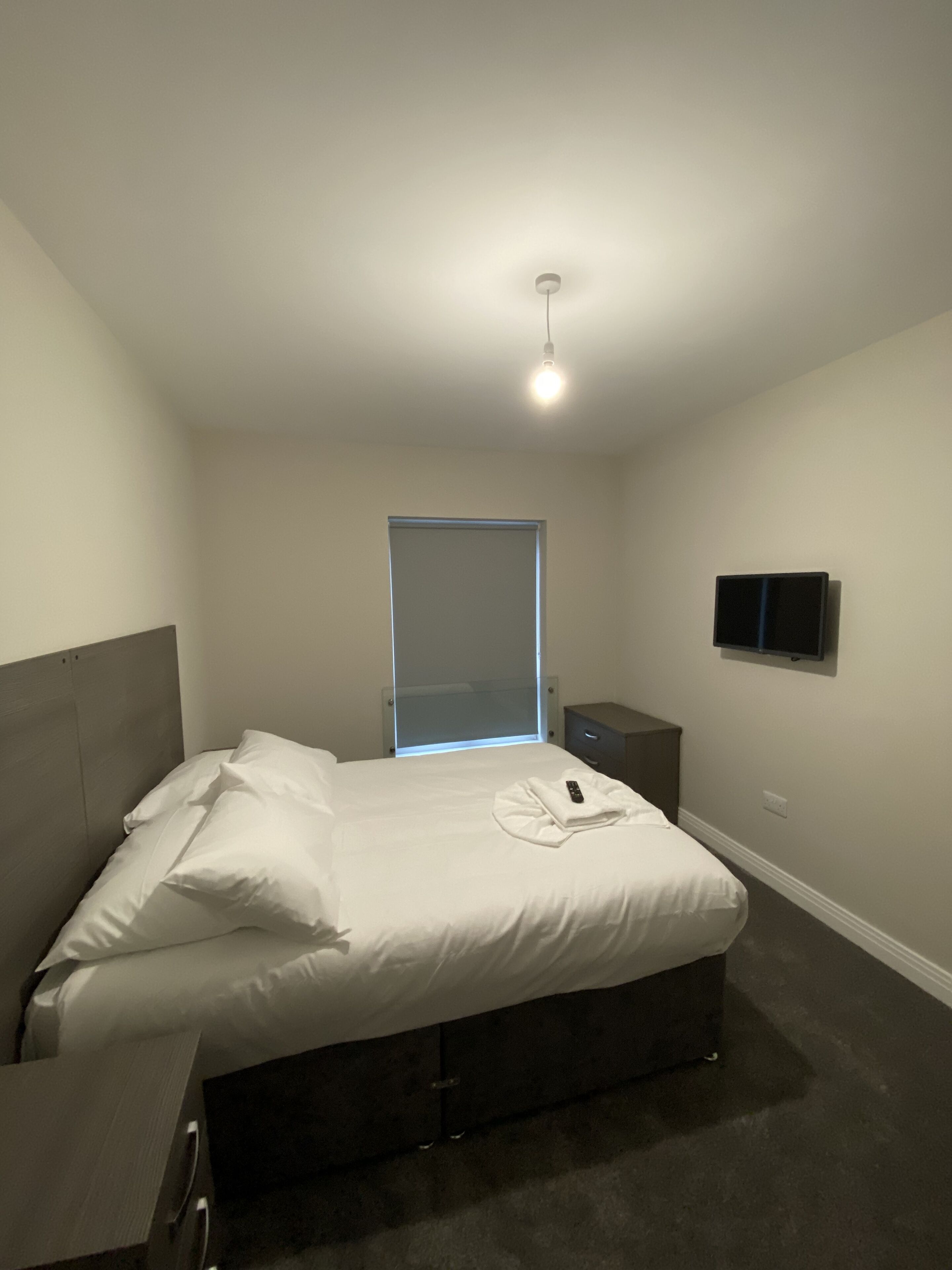 Un dormitorio con cama, mesita de noche y televisor montado en la pared.