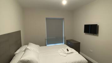 Un dormitorio con cama, mesita de noche y televisor montado en la pared.