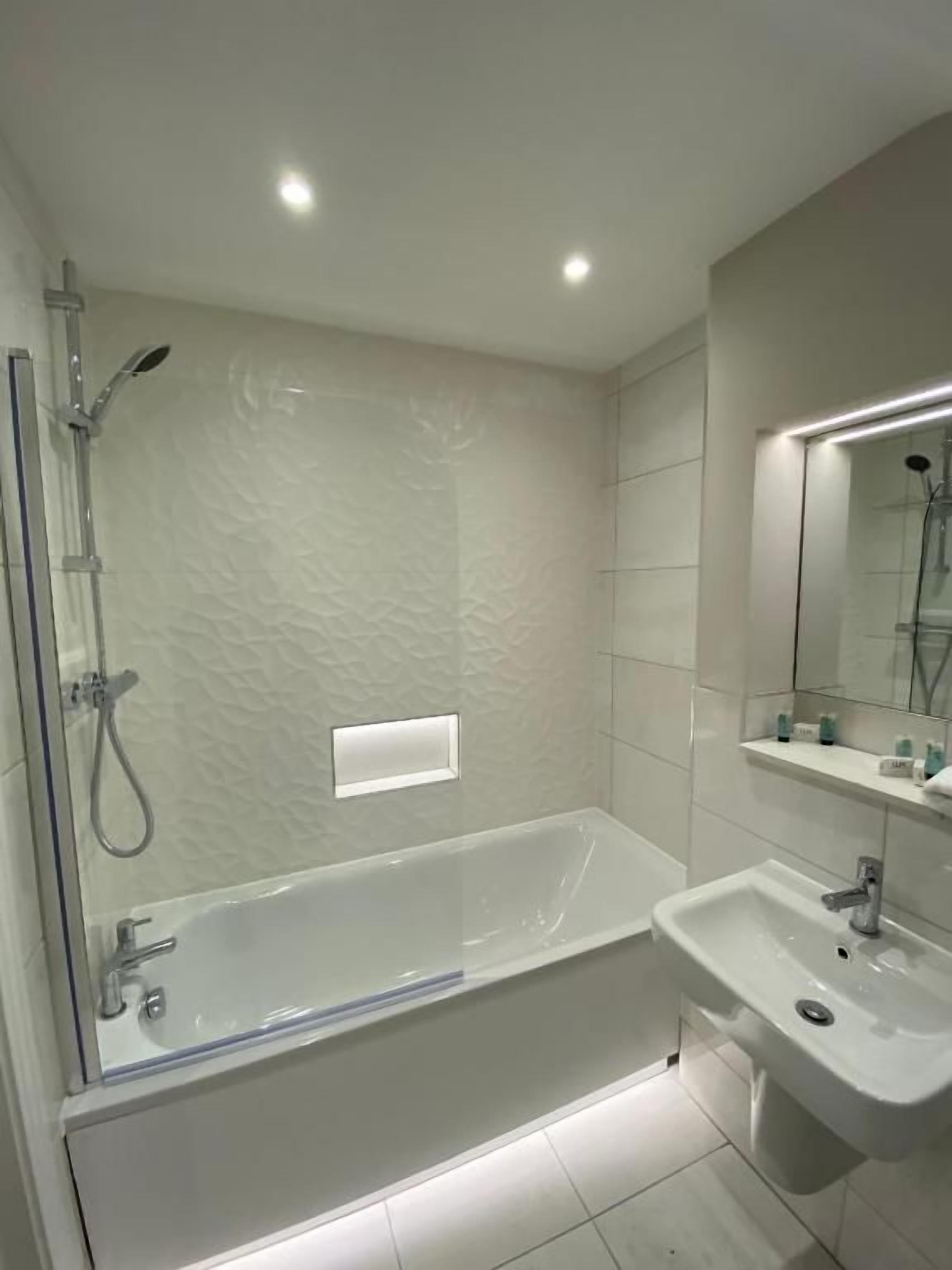 A modern bathroom with a glass-enclosed shower, a standalone bathtub, and a pedestal sink.