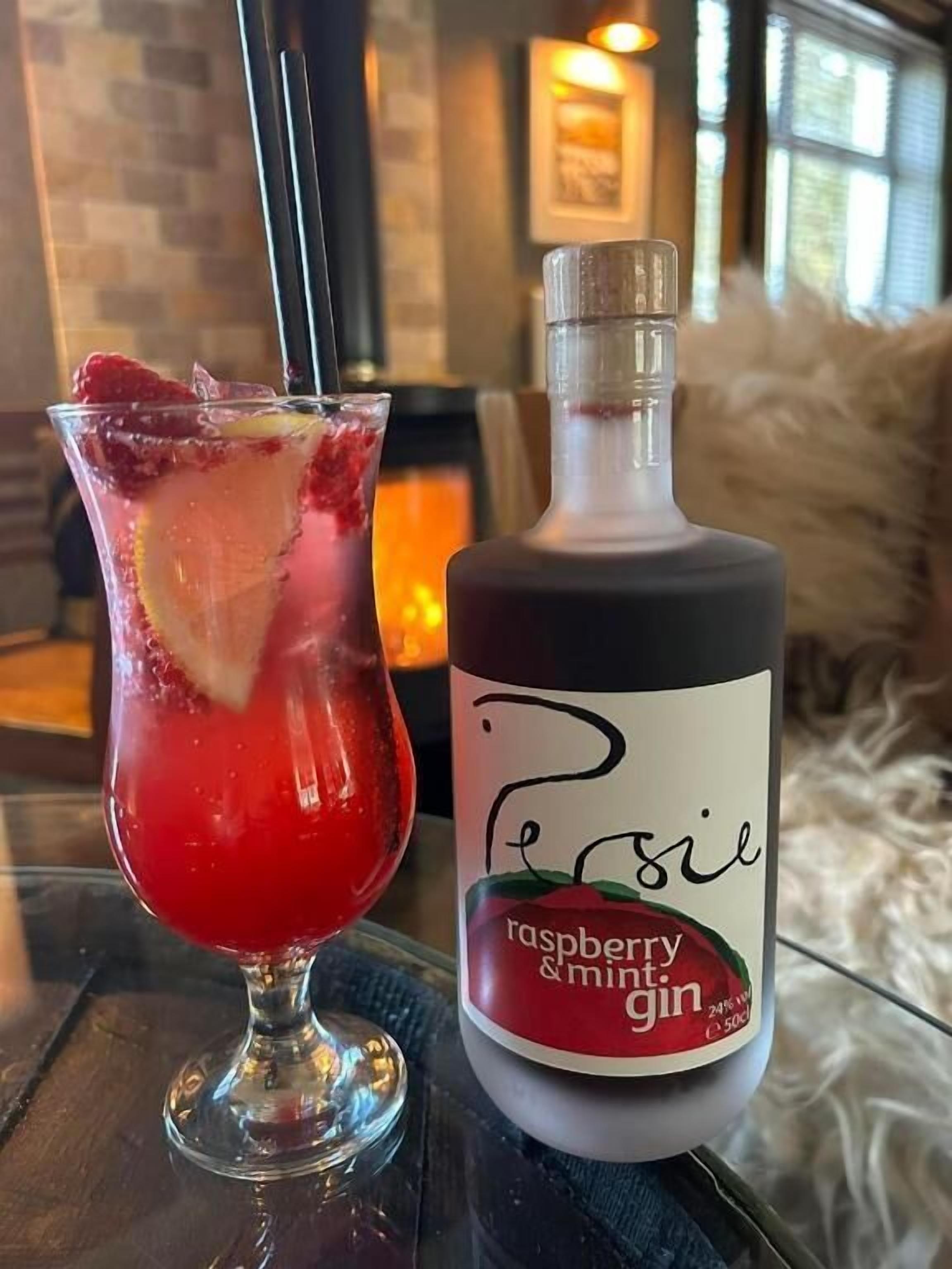 Un verre d’une boisson rouge, muni d’une paille, et une bouteille de gin à la framboise et à la menthe, posés sur une table.