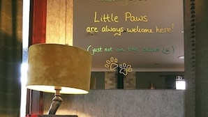 A cozy room with a sign welcoming dogs, a lamp, a book titled 'THE INN', and a pillow on a wooden table.