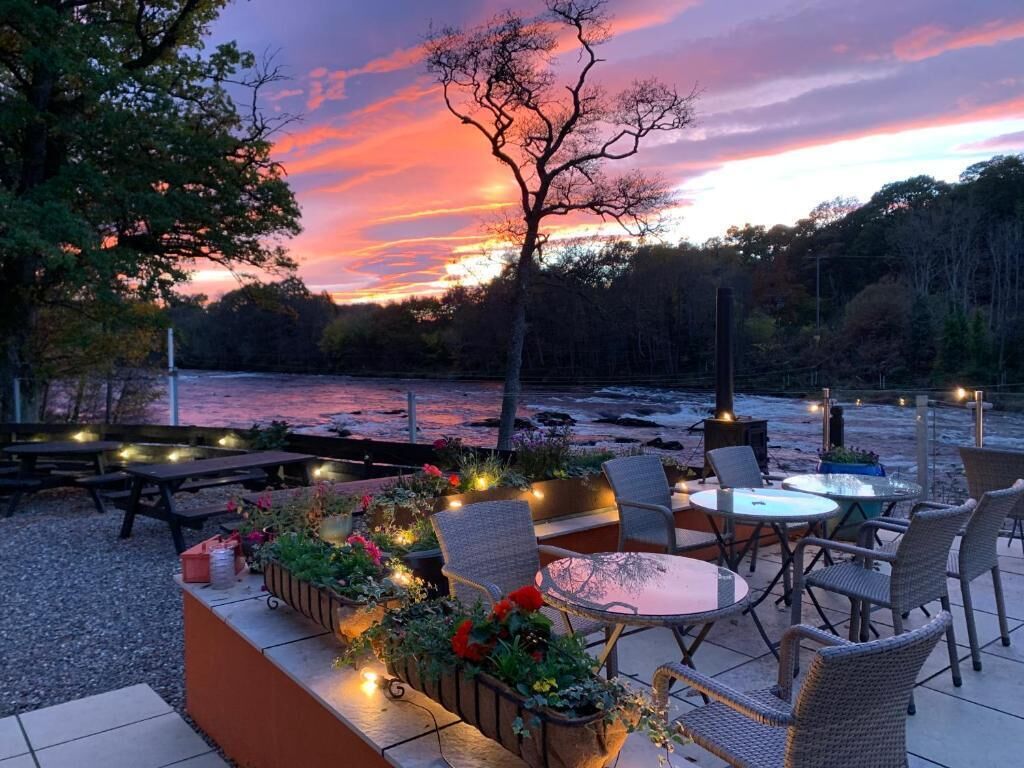 Un espace extérieur aménagé avec des tables et des chaises, offrant une vue sur une étendue d’eau et une zone boisée.