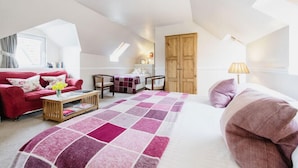 A spacious loft bedroom with a large bed, a red sofa, a wooden coffee table, and a view of the sky through a skylight.