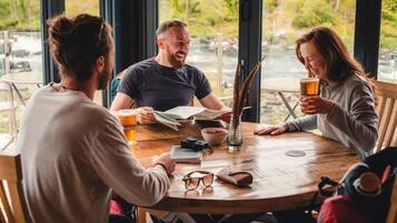 Three people seated around a round wooden table with a view of a river outside.