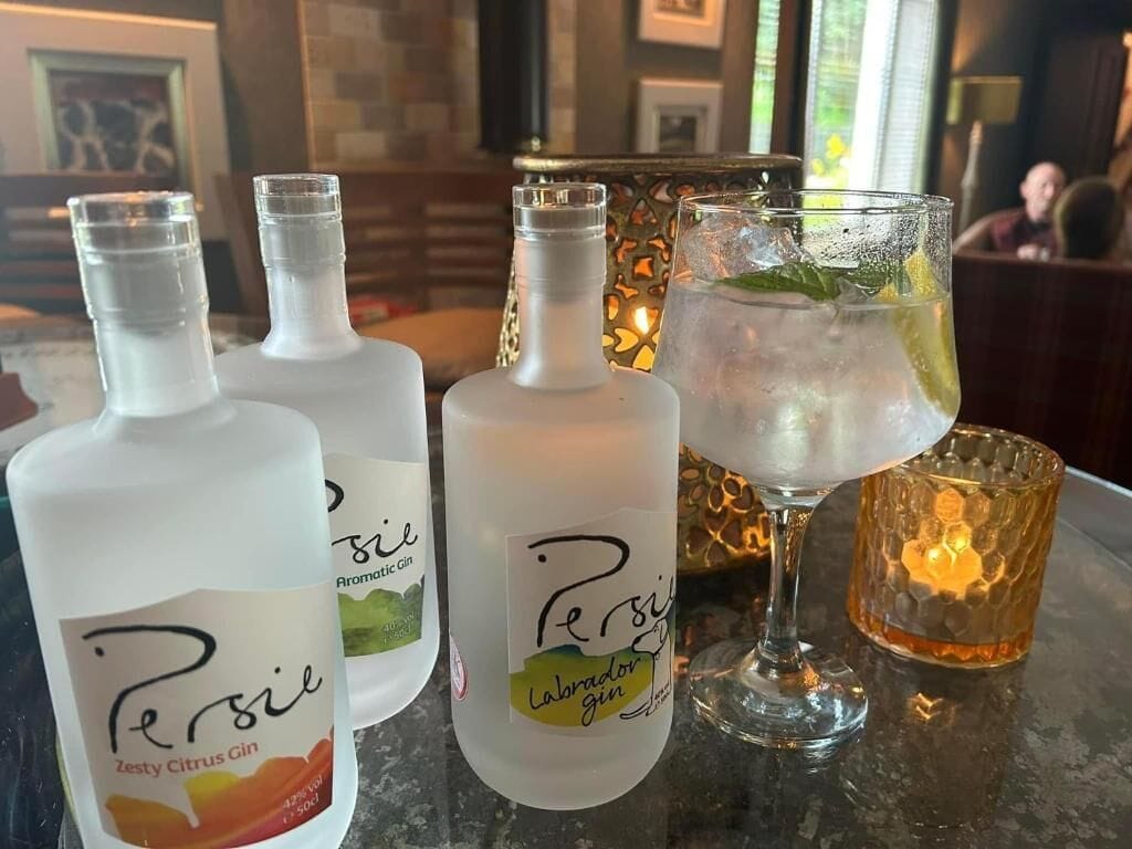Three bottles of Persie gin, a glass with a cocktail, and a candle on a bar counter.