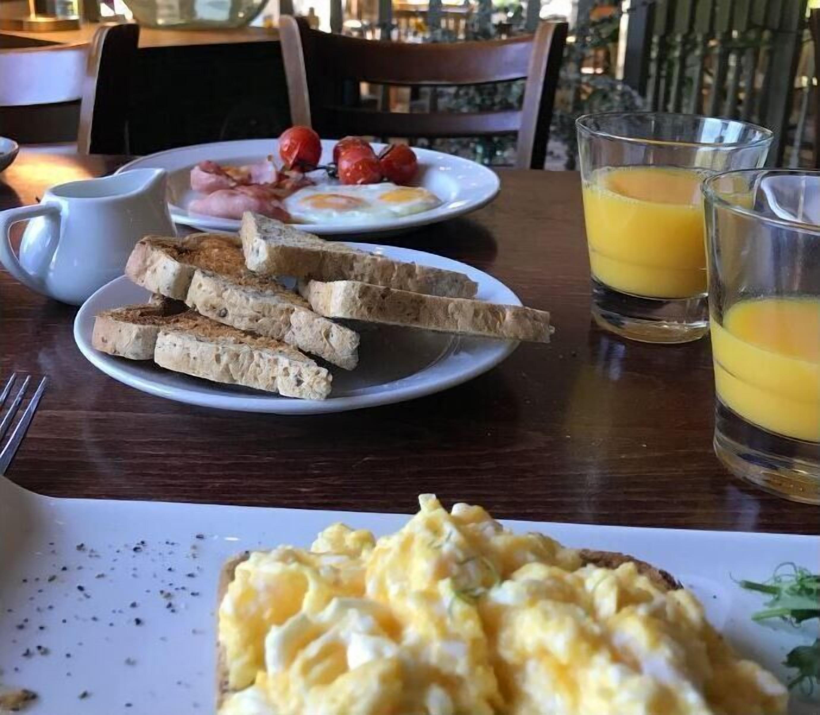 Une table dressée pour le petit-déjeuner, avec des toasts, des œufs brouillés, des tomates et du jus d’orange.