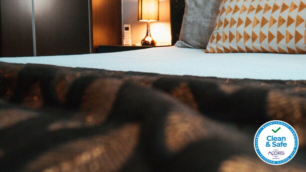 A hotel room with a bed, a nightstand with a lamp, and a pillow with a geometric pattern. - Vintage Place - Azorean Guest House (Ponta Delgada)