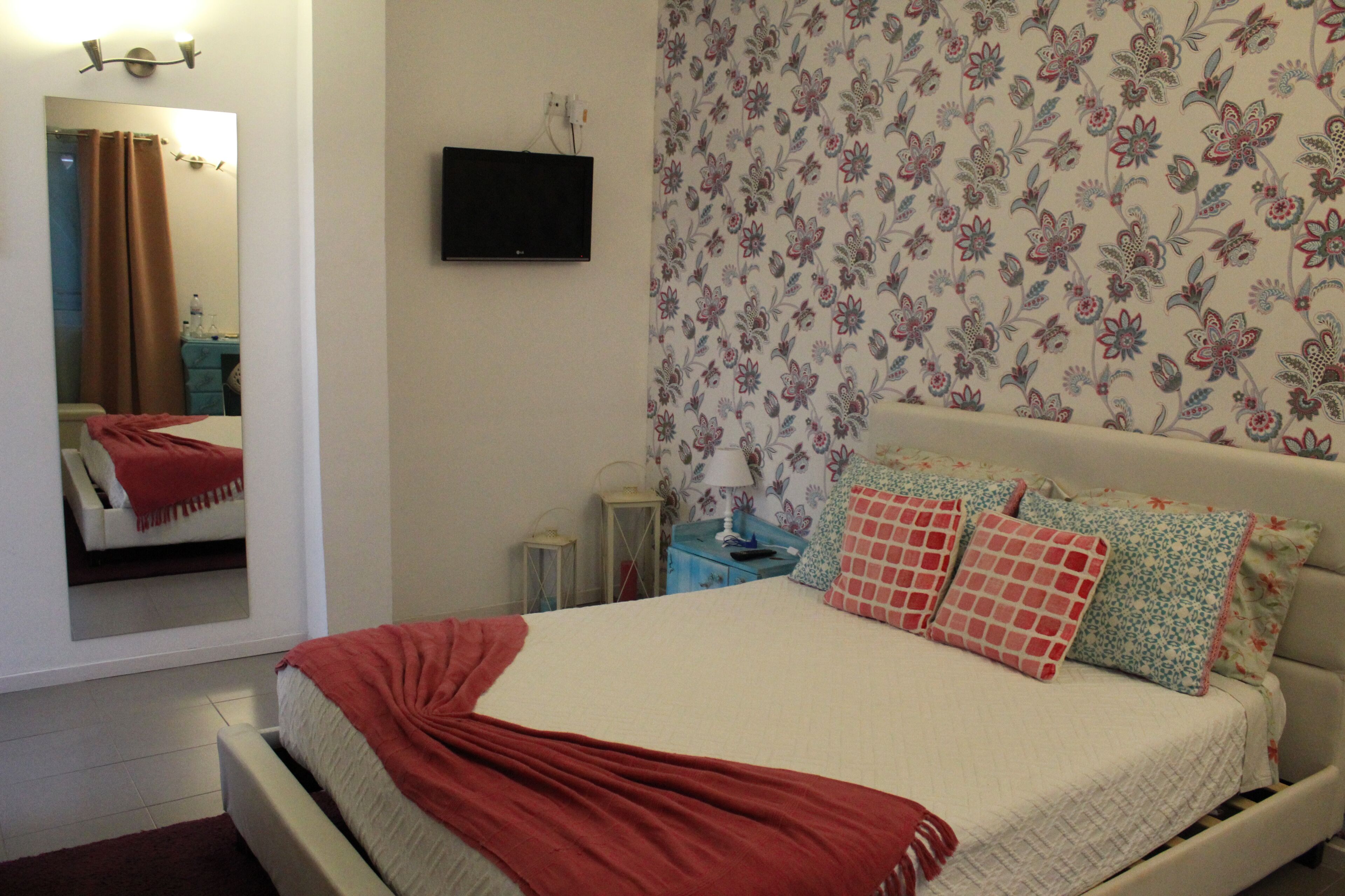 Un dormitorio con cama, televisión, espejo y papel tapiz con motivos florales.