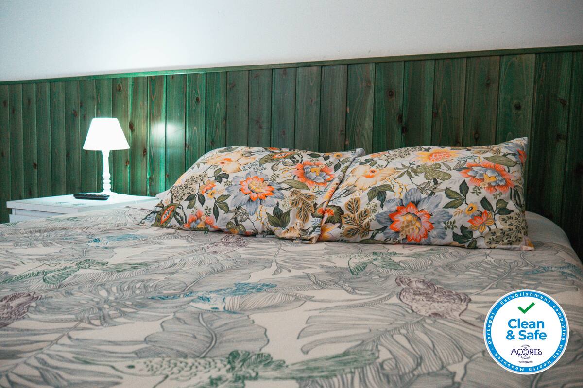 A bed with floral bedding and a pillow, a nightstand with a lamp, and a green wooden headboard.