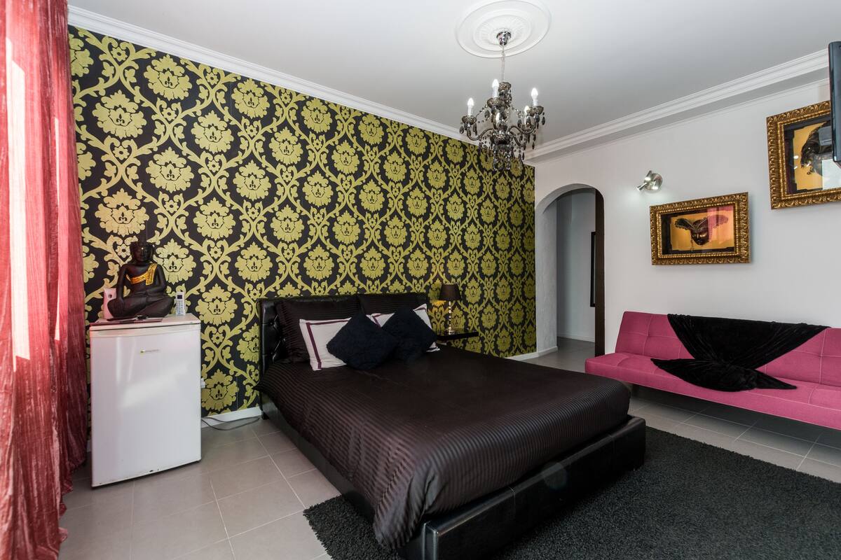 A bedroom with a bed, a dresser, a pink sofa, and a patterned wallpaper.