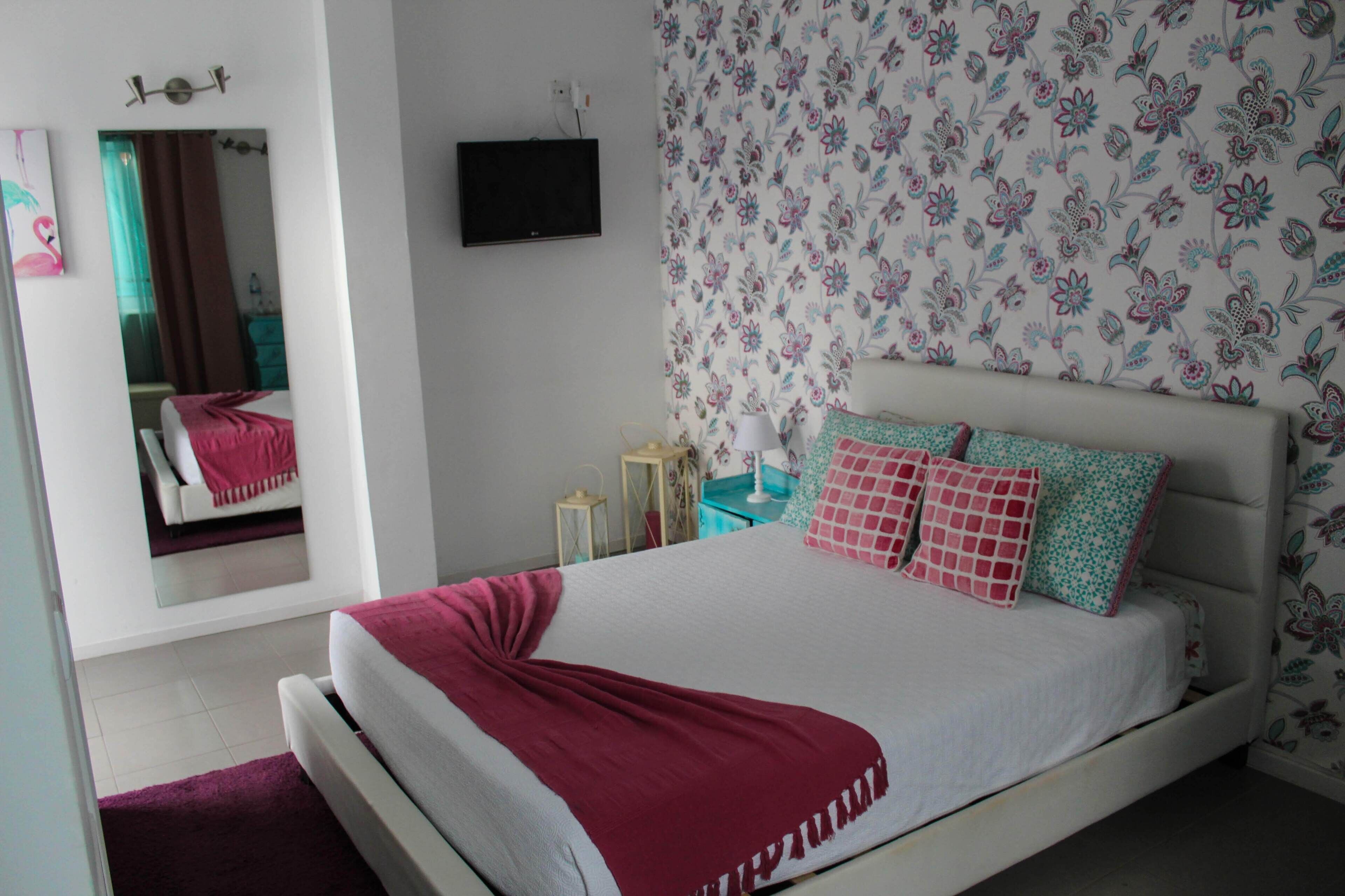 Een slaapkamer met een bed, een spiegel, een televisie en bloemenbehang.