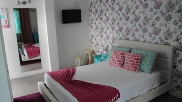 Een slaapkamer met een bed, een spiegel, een televisie en bloemenbehang.