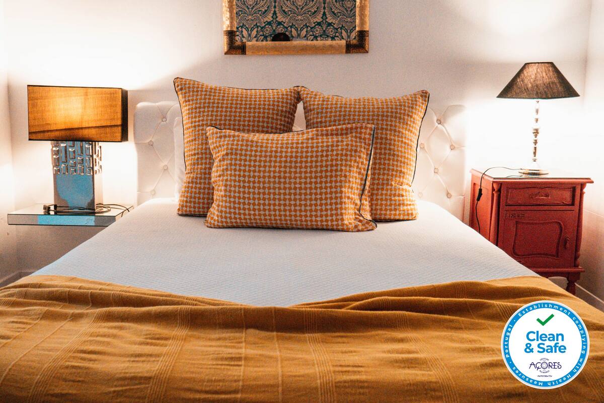 A neatly made bed with a checkered pillow set, a bedside lamp, and a nightstand with a lamp.