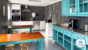 A modern kitchen with a wooden table and stools, a built-in oven, and teal cabinetry. - Vintage Place - Azorean Guest House (Ponta Delgada)