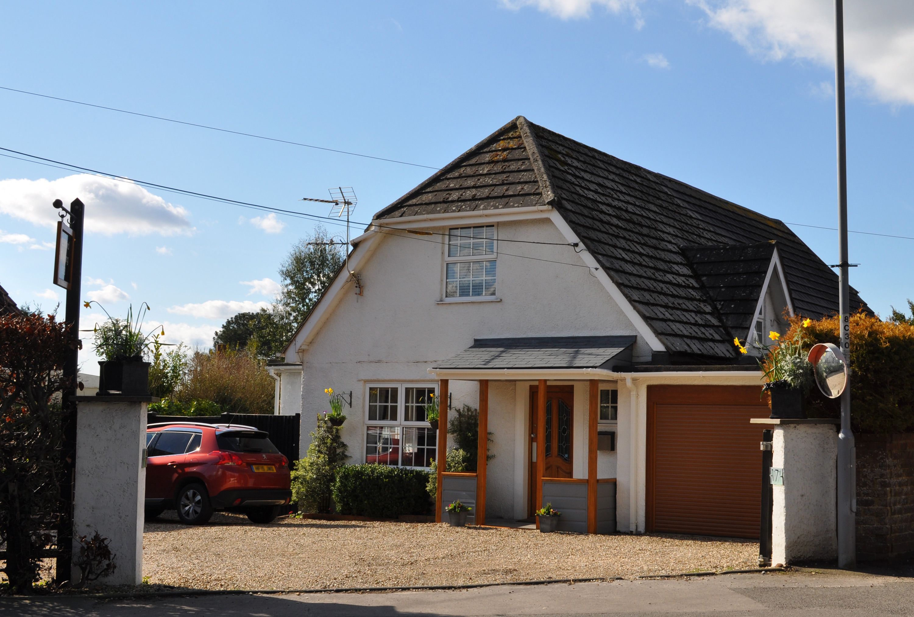 A single-story house with a sloped roof, a garage door, and a small porch area with potted plants.