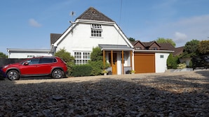 A house with a red car parked in the driveway, a garage, and a gravel front yard. - Canford Crossing (Wimborne)