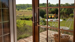 A view from a room through a glass door, featuring a wooden deck with outdoor furniture, a table with drinks, and a basket. - Chanticleer Guest House (Sturgeon Bay)