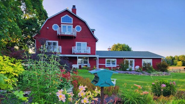 A red house with a balcony, surrounded by a well-maintained garden with various plants and flowers. - Chanticleer Guest House (Sturgeon Bay)