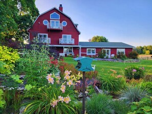 Una casa roja con balcón, rodeada de un jardín bien cuidado con diversas plantas y flores.