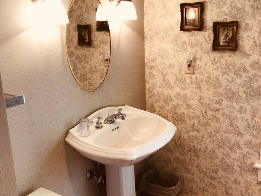 Een badkamer met een wastafel op voet, twee wandlampen, een spiegel en een klein afvalbakje.