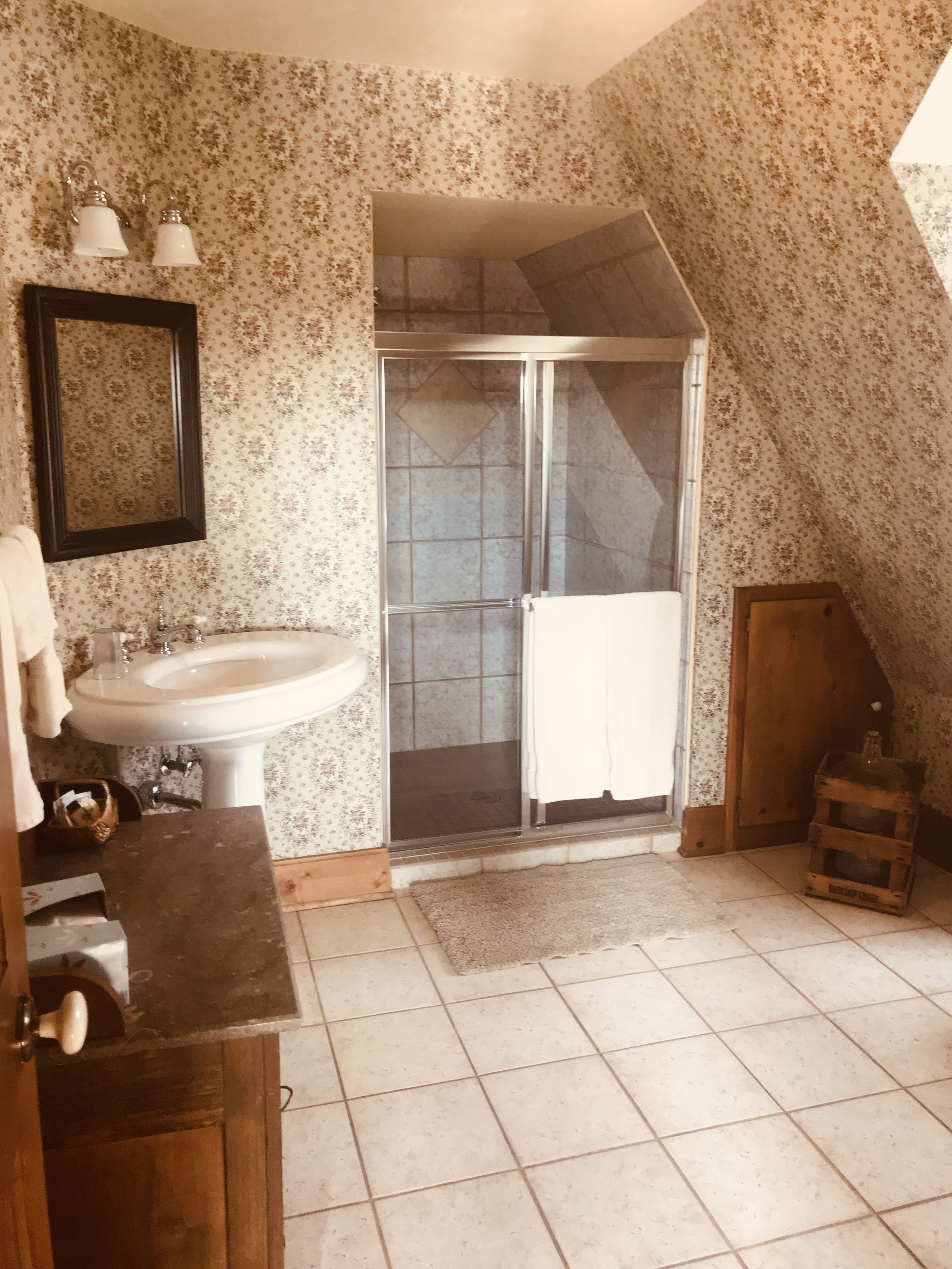 Un baño con lavamanos, espejo, ducha y armario de madera.