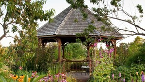 A gazebo with a tiled roof surrounded by lush greenery and flowering plants. - Chanticleer Guest House (Sturgeon Bay)