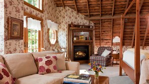 A cozy room with a fireplace, a sofa, a plaid chair, and a bed. - Chanticleer Guest House (Sturgeon Bay)