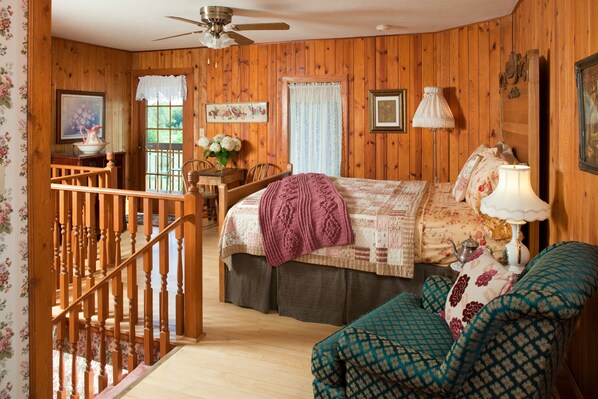 Habitación con paneles de madera, una cama, una silla, una mesa y una escalera.