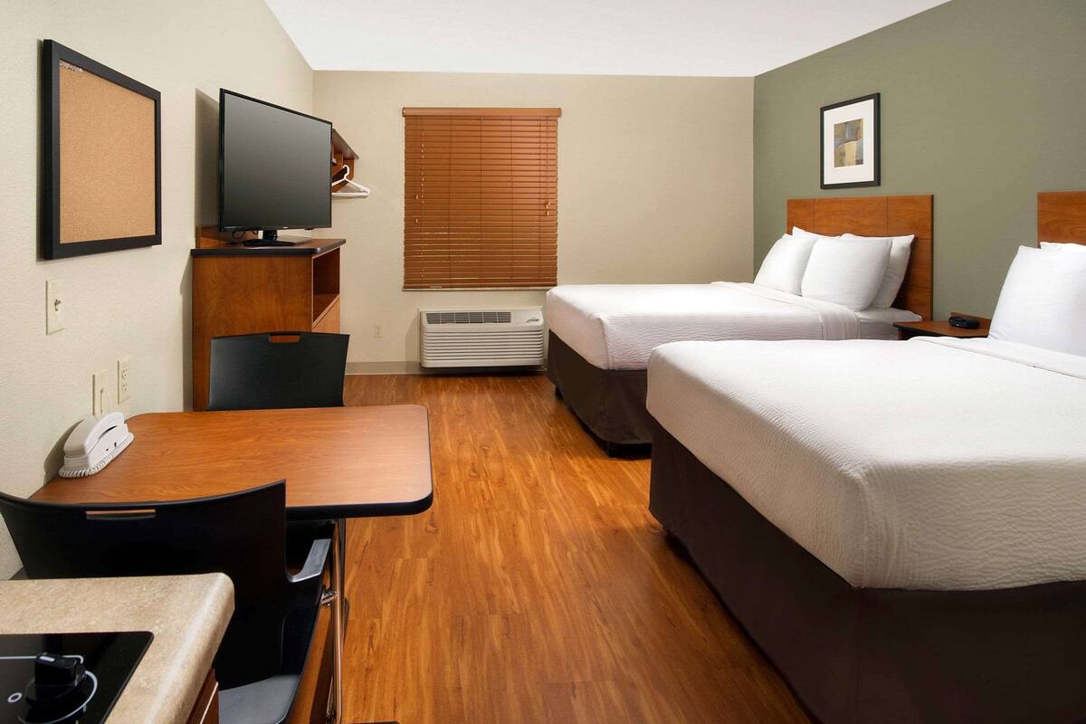 A hotel room with two beds, a desk, a chair, a television, and a window with blinds.