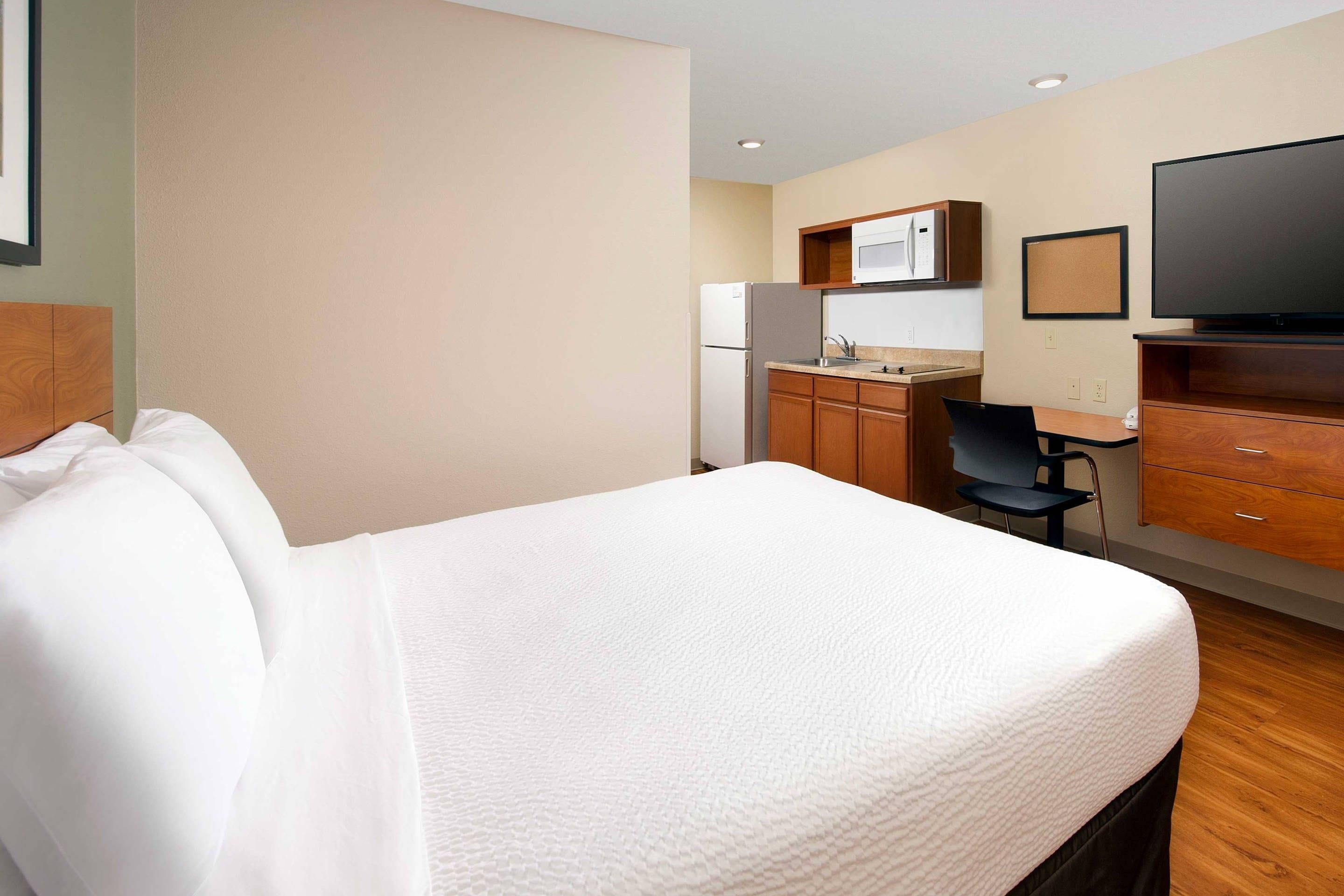 A hotel room with a bed, a desk, a chair, a television, and a kitchenette.