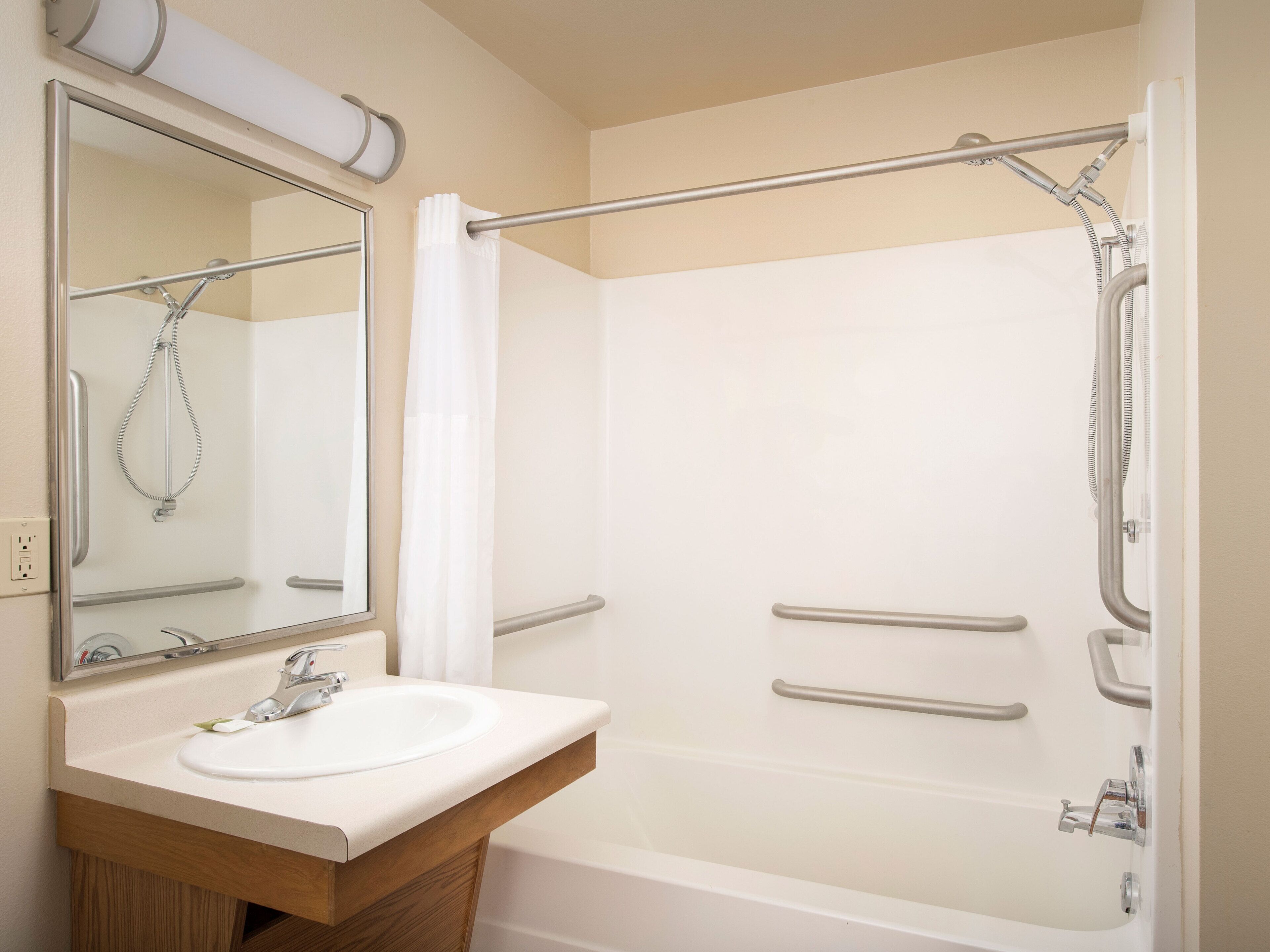 A bathroom with a sink, mirror, shower, and grab bars.