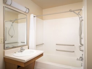 A bathroom with a sink, mirror, shower, and grab bars.