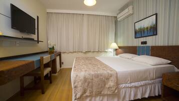 A hotel room with a bed, desk, chair, TV, and artwork on the wall.