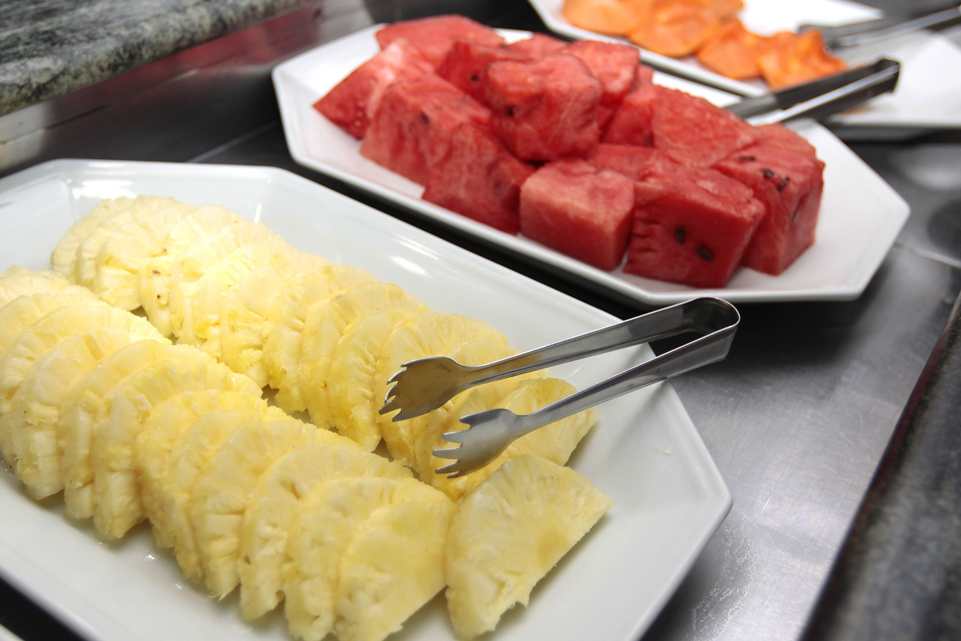 Une table de buffet avec des assiettes remplies de tranches d’ananas et de pastèque.