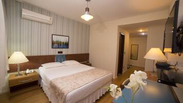 Quarto de hotel com uma cama grande, duas luminárias de cabeceira, uma TV de tela plana e um ar condicionado fixado na parede.