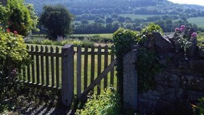 A stone wall with a wooden gate, lush greenery, and a view of rolling hills in the distance. - Upper Letton Farmhouse (Bucknell)