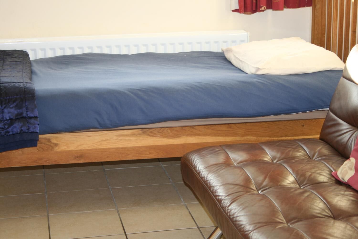 A bedroom with a bed, a wooden headboard, a brown leather sofa, and a radiator.