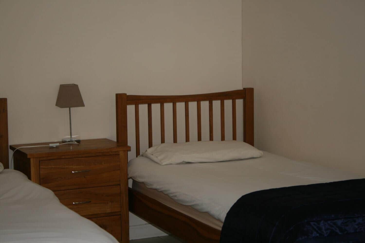 Una cama individual con cabecera de madera, una mesita de noche con lámpara y un aparador con cajones.