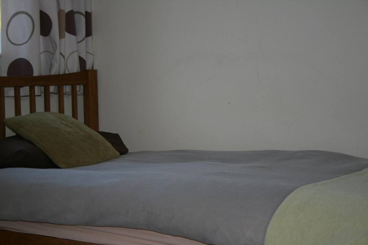 A bed with a wooden headboard, grey bedding, and a green pillow.