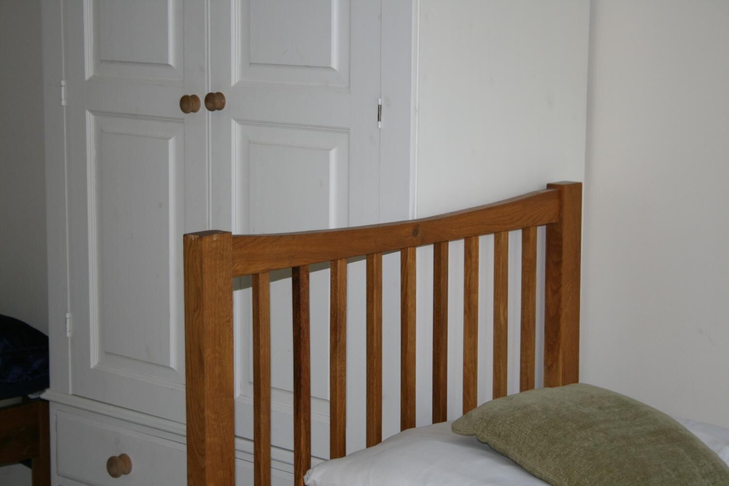 A wooden headboard with vertical slats, a white door with round knobs, and a green pillow on a bed.