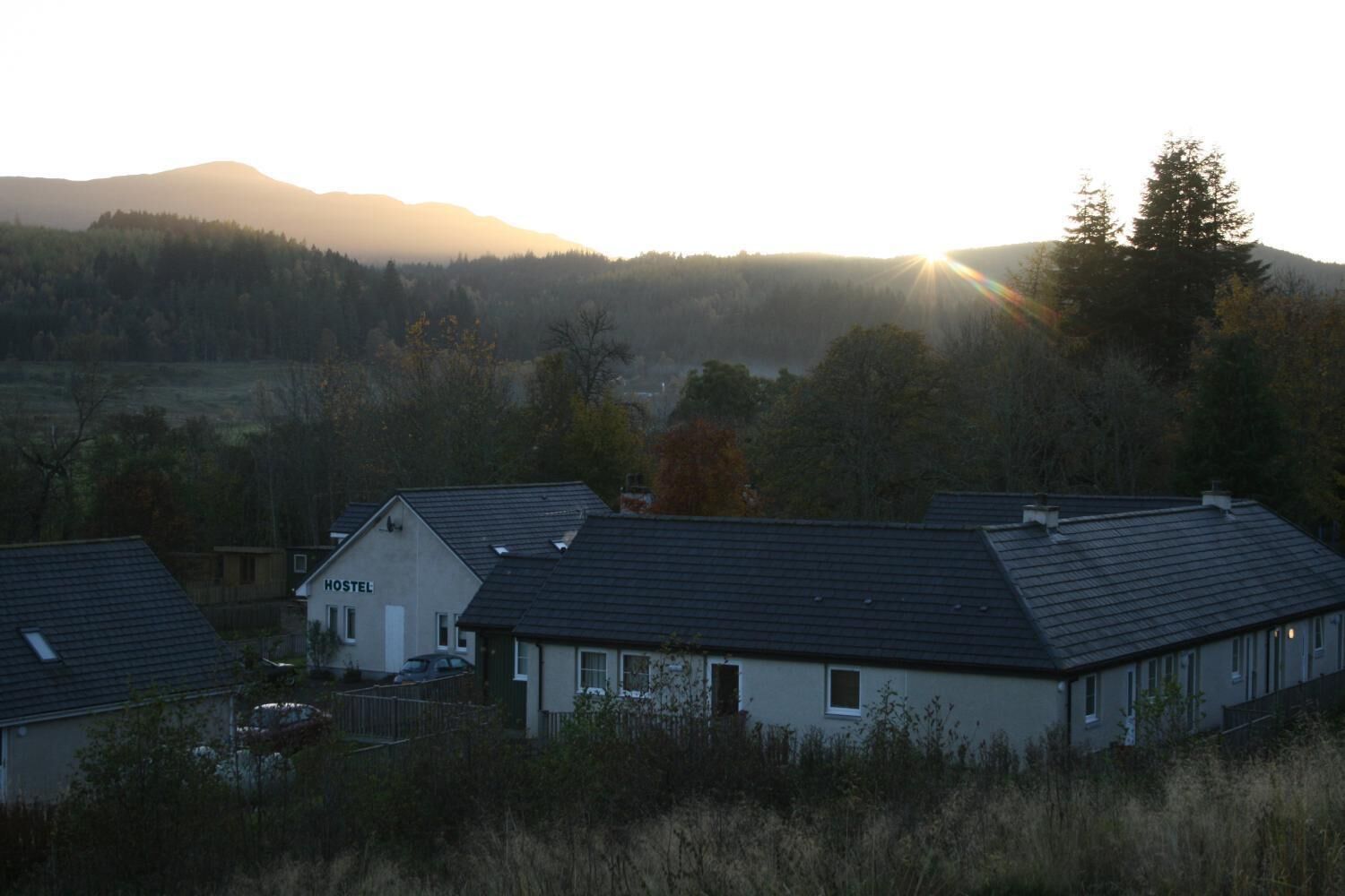 A hostel with a simple, functional design, surrounded by natural landscape and hills.