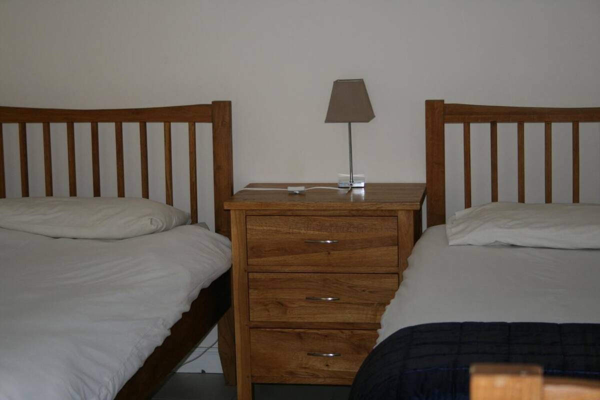 A room with two single beds, a wooden nightstand with a lamp, and a drawer unit.