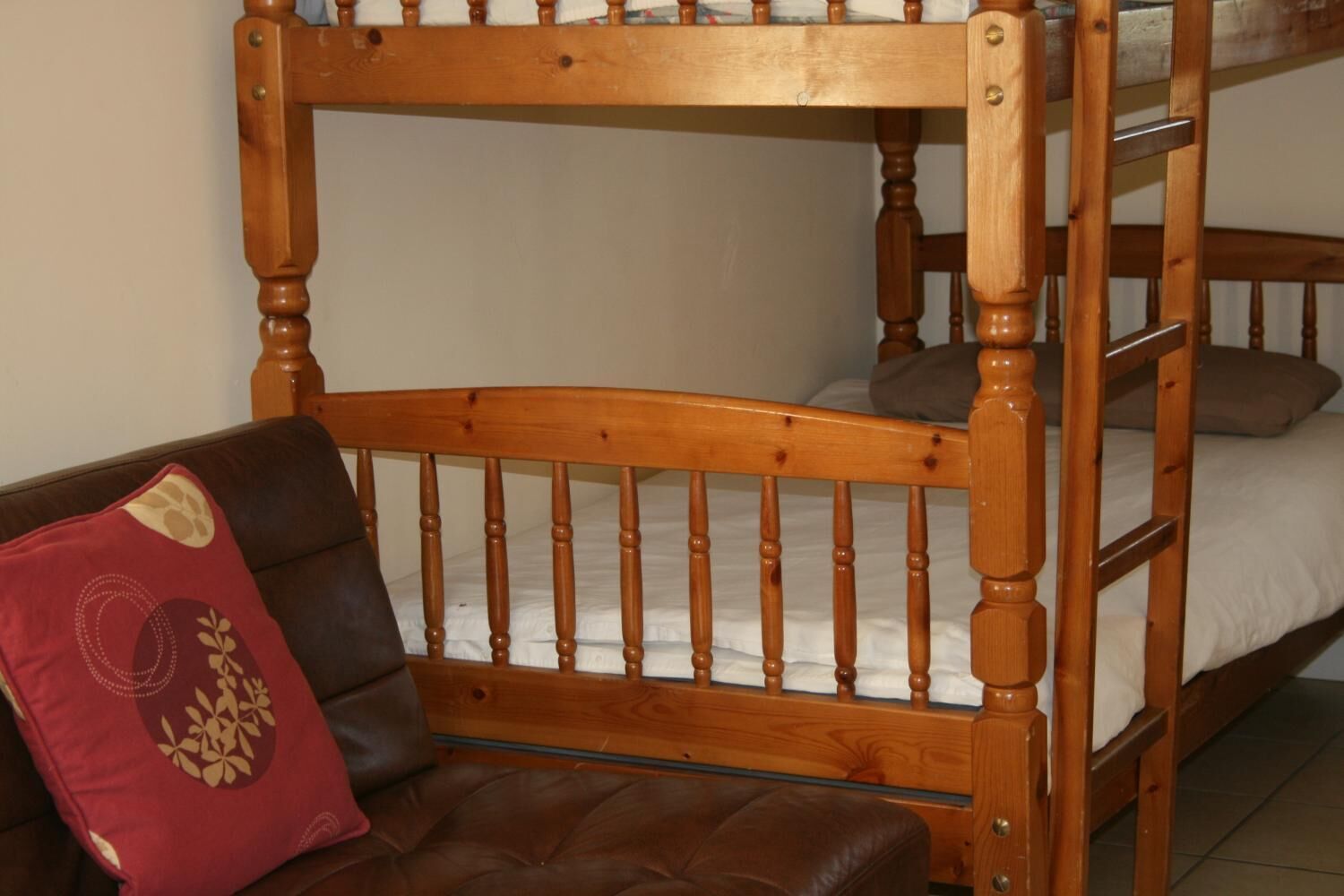 Ein Stockbett mit Holzrahmen und ein Ledersofa mit rotem Kissen.
