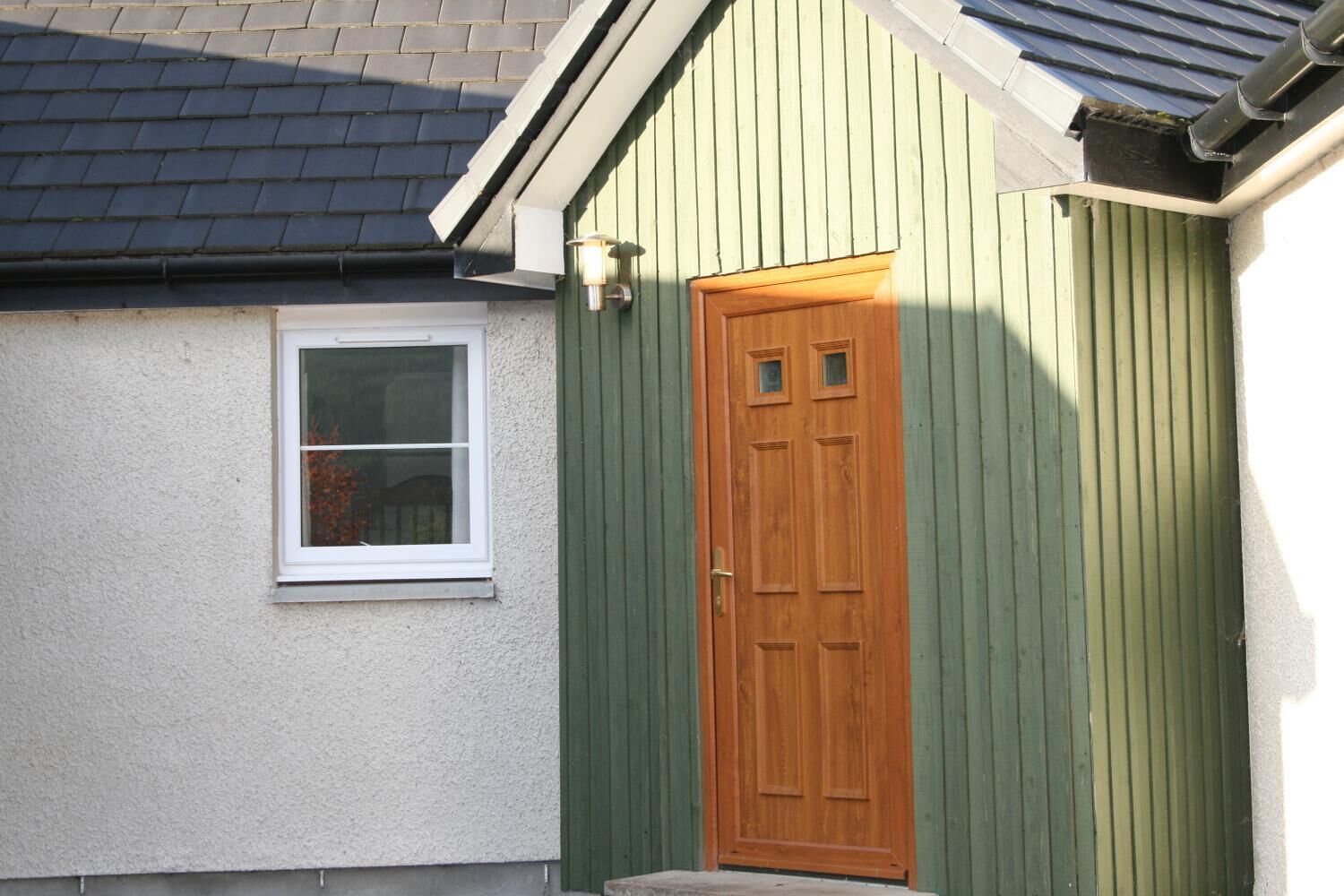 A house with a green exterior, a white window, and a wooden door.