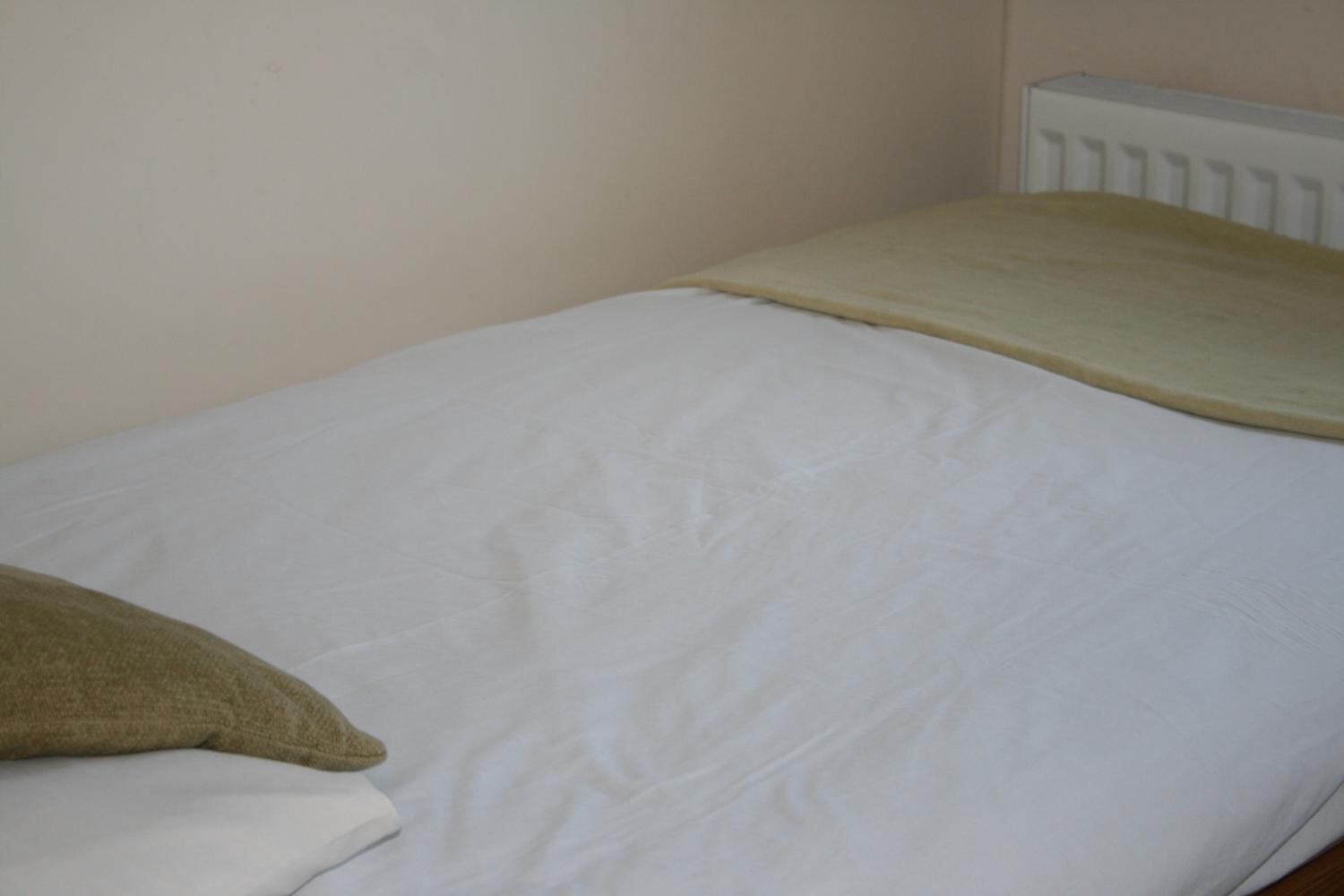A single bed with a white mattress and a beige blanket.