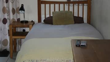 Un dormitorio con una cama, una mesita de noche, una lámpara y un control remoto sobre una mesa de madera.