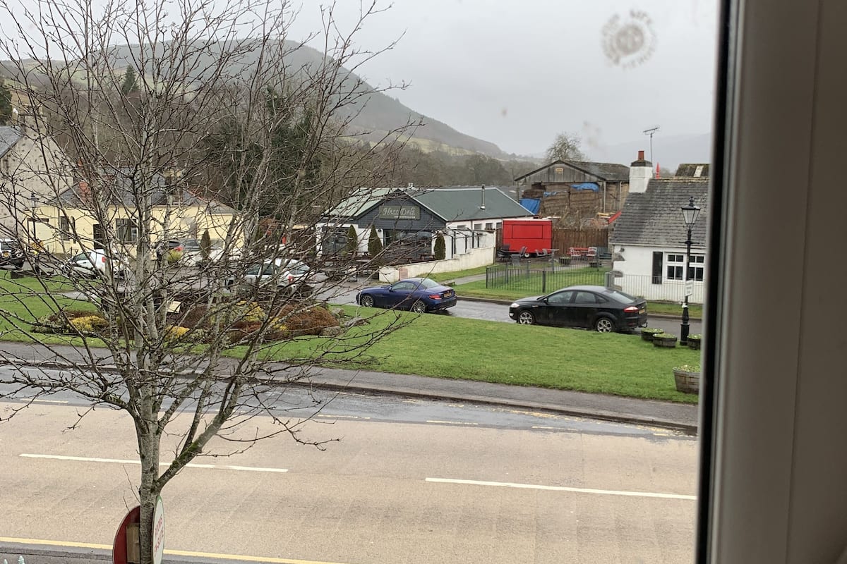 A view from a window overlooking a parking lot with cars, a tree, and buildings in the background.