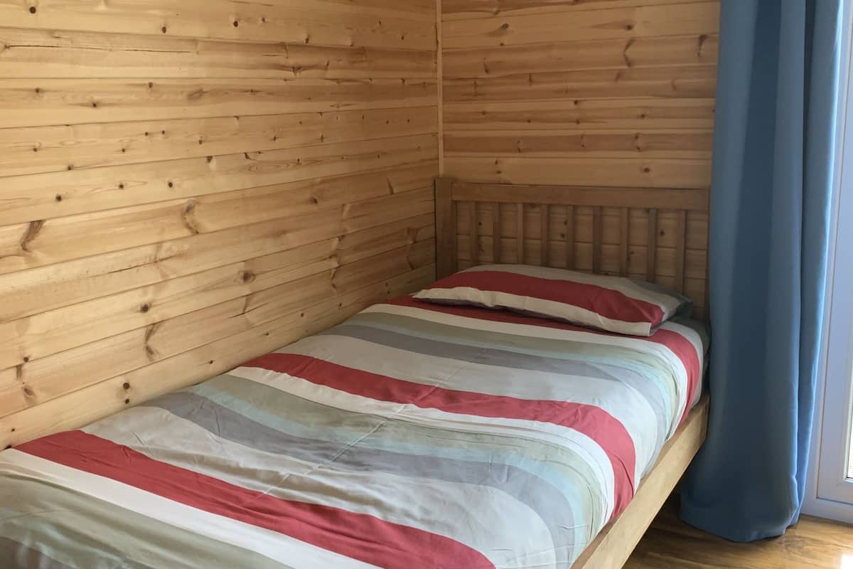 A single bed with a striped bedspread in a room with wooden panel walls and a wooden floor.