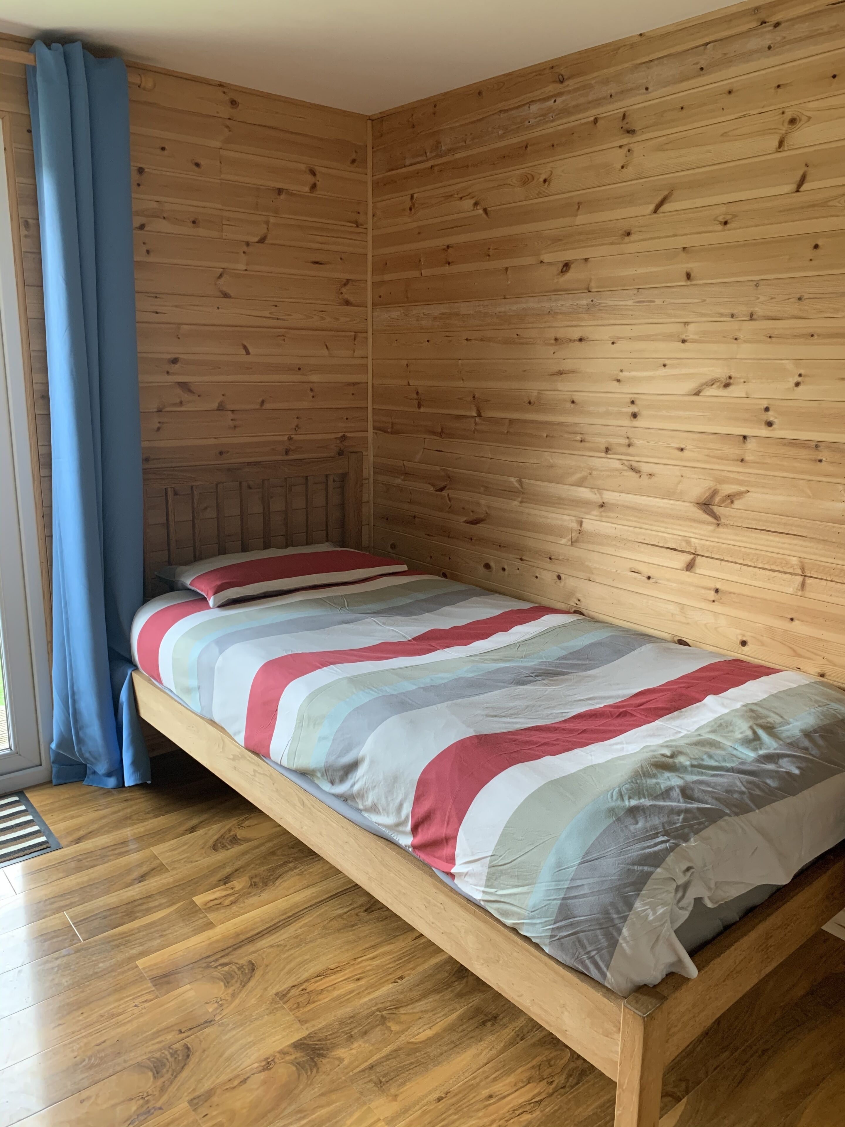 Een enkel bed met een gestreept dekbed in een kamer met houten wanden en een houten vloer.